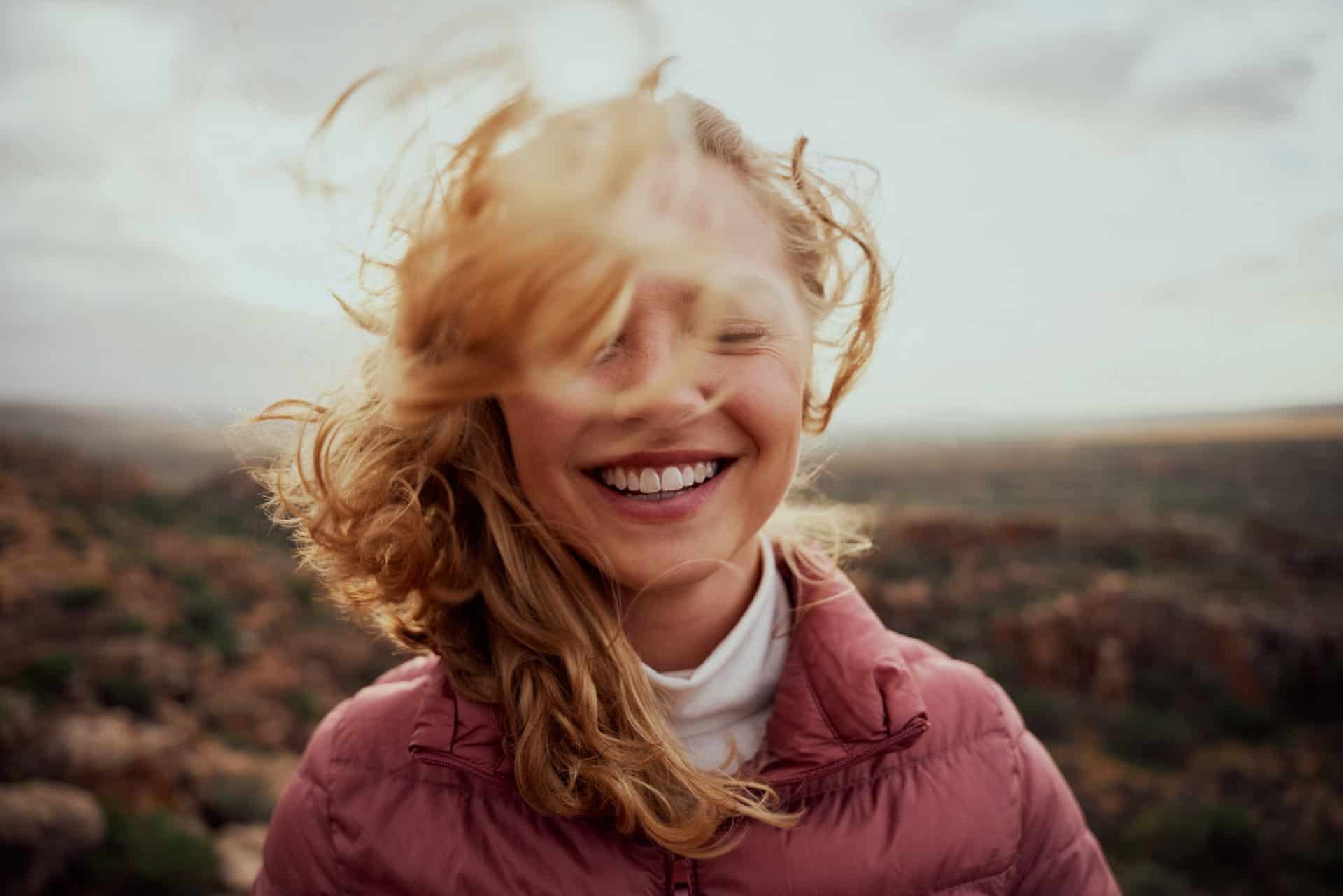 Young woman, smiling, with face partially covered by wind-blown hair